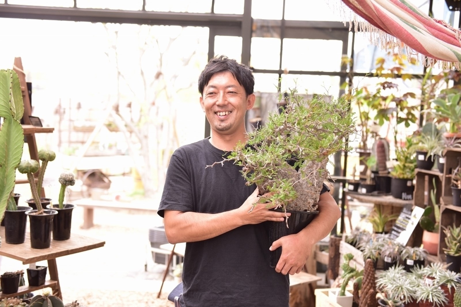 温室で大きな多肉植物を抱えて笑う男性社員の写真