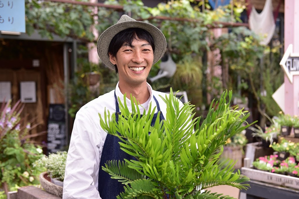 観葉植物を抱えて笑顔を見せる社員の写真